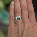 1.22ct Deep Teal Montana Sapphire With Bezel Set Diamond Halo In 18k Yellow Gold on the hand