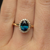 1.55ct Oval Blue Nigerian Sapphire and Diamond Four Prong Halo Ring in 14k Yellow Gold on hand