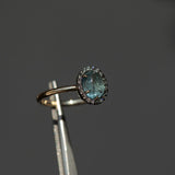 2.40ct Oval Cabochon Montana Sapphire and Antiqued Six Prong Low Profile Halo Ring in 14k Yellow Gold in tweezers