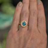 1.22ct Deep Teal Montana Sapphire With Bezel Set Diamond Halo In 18k Yellow Gold on the hand