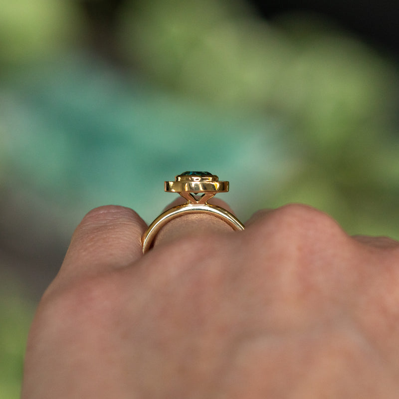 1.22ct Deep Teal Montana Sapphire With Bezel Set Diamond Halo In 18k Yellow Gold on the hand