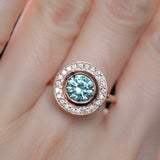 1.95ct Teal Montana Sapphire With Bezel Set Diamond Halo In 14k Rose Gold on hand